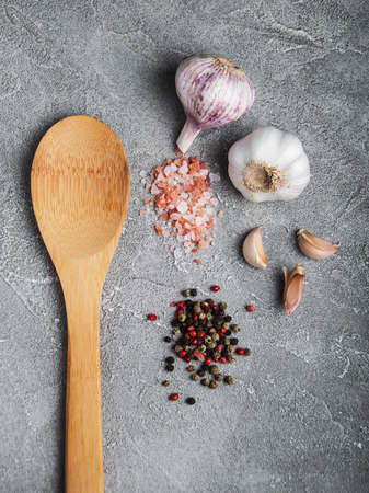 Wooden spoon with garlic, salt and pepper on a gray stone backgroundの写真素材