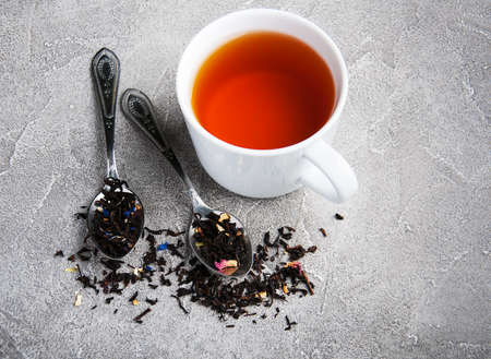 Tea cup and assortment of dry tea in spoons on a gray  stone background