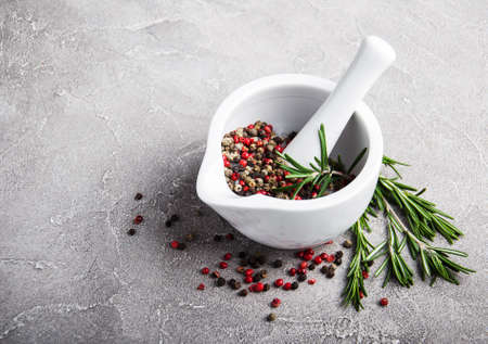 Pepper in white mortar and rosemary on a gray stone background