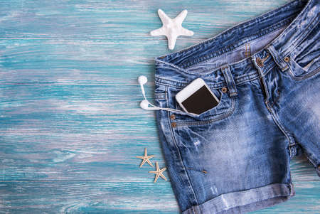 Summer  accessories: denim shorts, mobile phone, headphones, shells on a wooden backgroundの写真素材