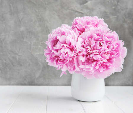 Vase with pink peony flowers on a white wooden table