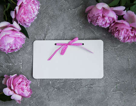 invitation card and pink peony flowers on a stone background