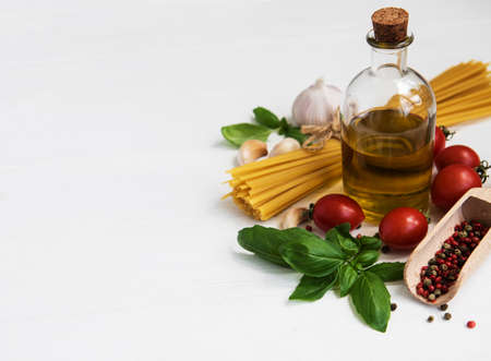 Italian food ingredients, olive oil, spices, pasta and tomatoes on a white wooden tableの写真素材