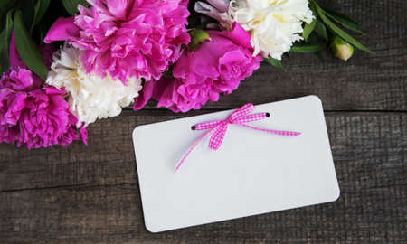 invitation card and pink peony flowers on a old wooden backgroundの写真素材