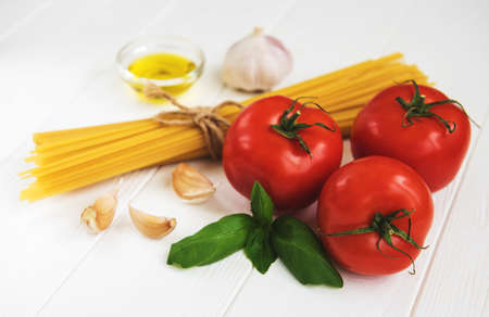 Italian food ingredients, pasta, basil  and tomatoes on a white wooden tableの写真素材