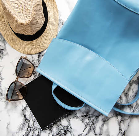 Blue  leather backpack with hat,  notebook and glasses on a marble background
