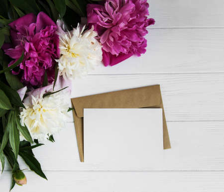 invitation card, craft envelope and pink peony flowers on a white wooden backgroundの写真素材