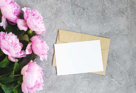 invitation card, craft envelope and pink peony flowers on a stone background