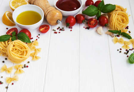 Italian food ingredients, olive oil, spices, pasta and tomatoes on a white wooden tableの写真素材