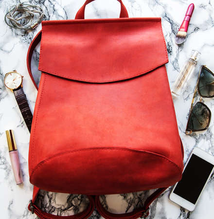 Red leather backpack with  accessories on a marble background