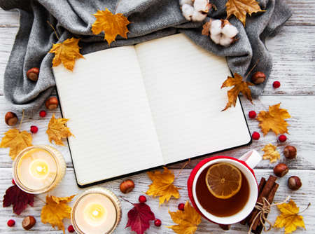 autumn flatlay on wooden backdrop with a notebook, cup of tea and fallen dry yellow leavesの写真素材