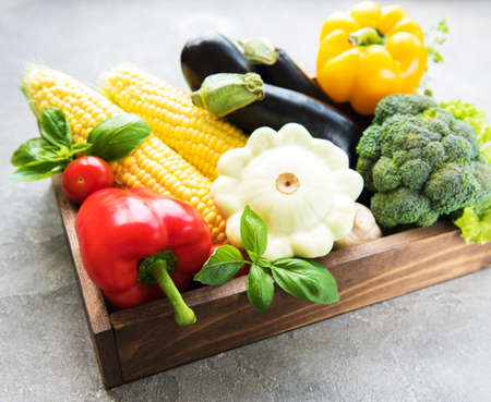 Box with different raw vegetables on a concrete background
