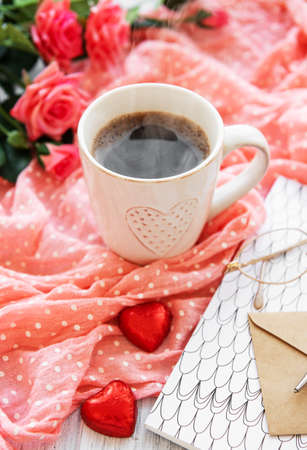cup of coffee with chocolate candies, roses and envelopeの写真素材