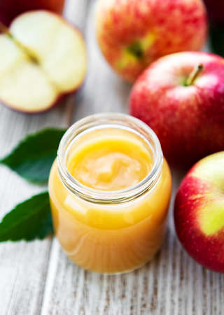 Applesauce in glass jar and fresh apples on a wooden tableの写真素材