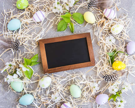 Easter eggs, straw and spring blossom on a concrete background