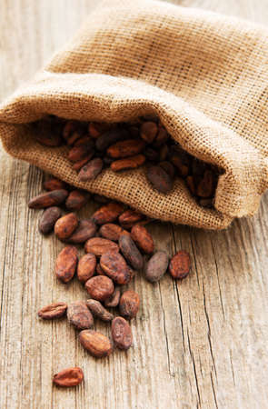 Raw cacao beans in burlap bag on a wooden tableの写真素材