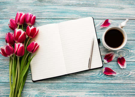 Notebook, cup of coffee  and pink tulips on a old wooden tableの写真素材