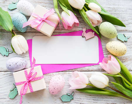 Gift boxes, easter eggs and tulips bouquet and greeting card on a old wooden background