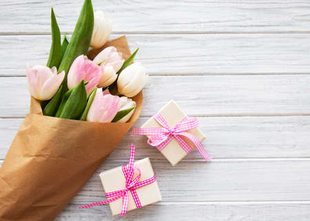 Gift boxes and tulips bouquet on a white wooden background