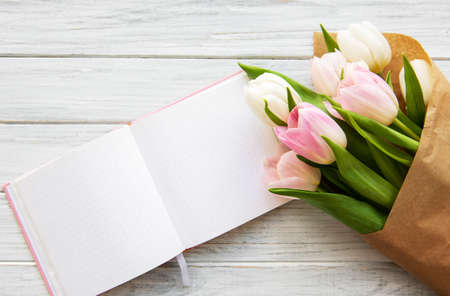 Workspace with notebook and pink tulips on a old wooden tableの写真素材