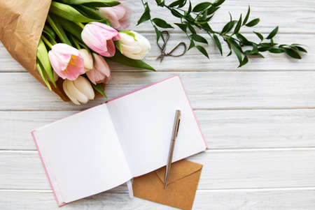 Workspace with notebook and pink tulips on a old wooden tableの写真素材