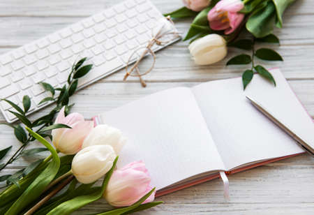 Workspace with keyboard, notebook and pink tulipsの写真素材
