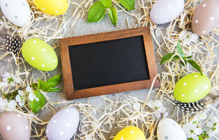 Easter eggs, straw and spring blossom on a concrete background