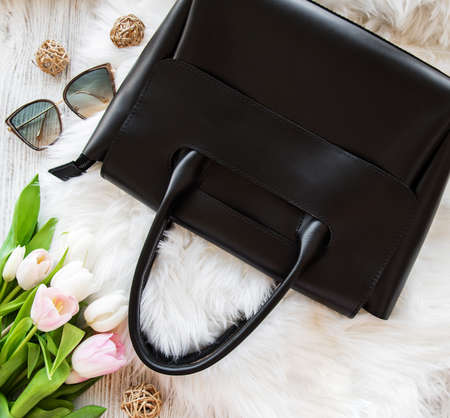 Black leather bag and flowers on a grey concrete background
