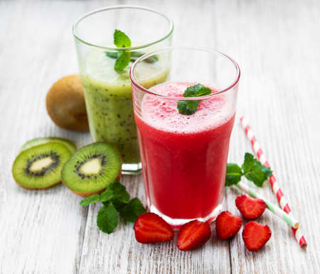 Kiwi and strawberry smoothies with fresh fruits on a old wooden tableの写真素材