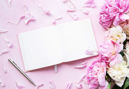 Open blank notebook with pen and pink peonies on a pink concrete backgroundの写真素材