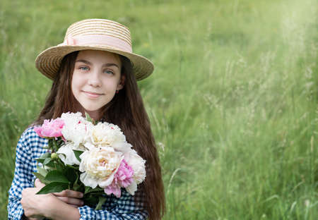 Girl in a summer field with a straw hat and a bouquet of peoniesの写真素材