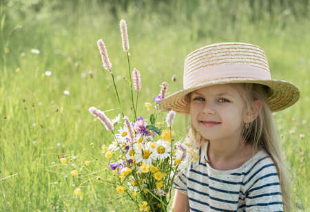 Cute little girl with blond hair in a summer field with a straw hatの写真素材