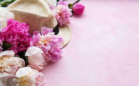Holiday summer background. Pink peonies and hat on a pink concrete background.の写真素材
