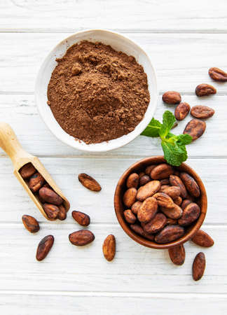 Bowl with Cocoa powder and beans on a white wooden  backgroundの写真素材