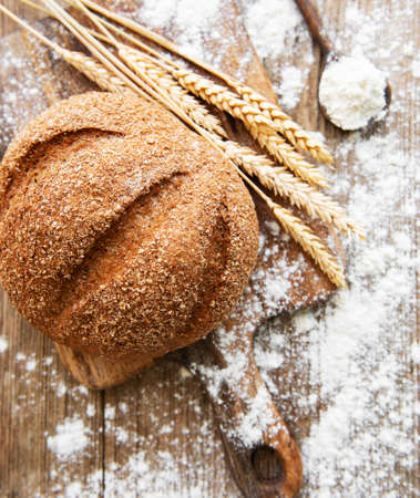 Bread with wheat ears and flour on old wooden table