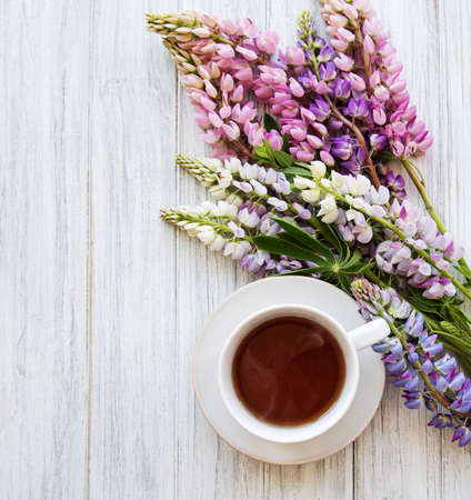 Pink and purple lupine flowers and cup of tea on a old wooden tableの写真素材