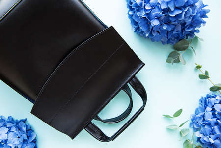 Black leather backpack with blue hydrangea flowers   on a light blue  background.の写真素材
