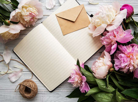 Flat lay blogger or freelancer workspace with a  notebook, pink peonies on a white wooden tableの写真素材