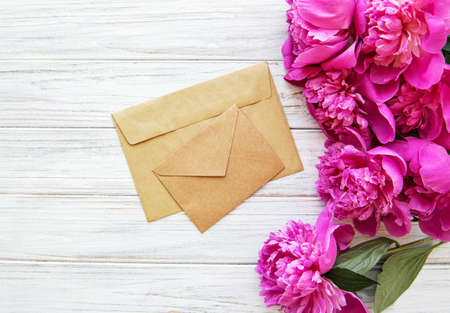 Wedding invitation and envelope with pink peonies on a old white wooden background
