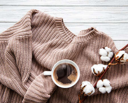 Autumn and winter home still life . The view from the top. The concept of home atmosphere and decor. Cup of coffee, cotton flowers, sweater and autumn leaves on a white wooden backgroundの写真素材