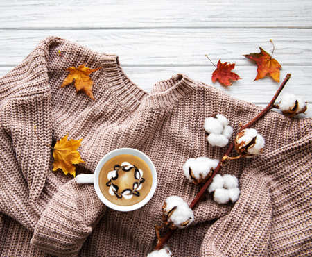 Autumn and winter home still life . The view from the top. The concept of home atmosphere and decor. Cup of coffee, cotton flowers, sweater and autumn leaves on a white wooden backgroundの写真素材