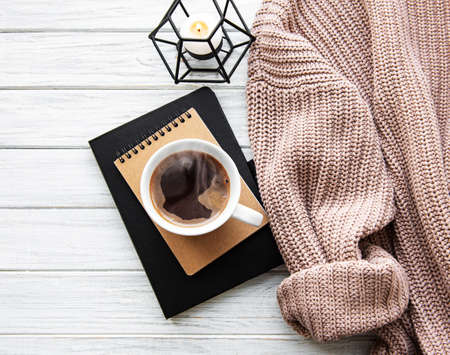 Autumn and winter home still life . The view from the top. The concept of home atmosphere and decor. Cup of coffee, notebooks, sweater and autumn leaves on a white wooden background の写真素材