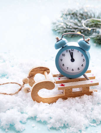 Christmas alarm clock on a wooden sled in the snow shows the time midnight.
