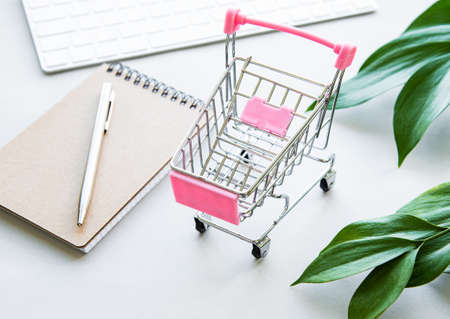 Online shopping. Laptop, shopping cart on white background with green leaves. The concept of unity with nature. Eco still life. Top viewの写真素材