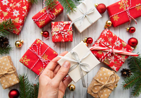 Christmas background with gift boxes and decorations on white wooden table. Woman's hands holding gift box.の写真素材