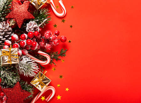 Christmas and New year background with fir branches, holly berry,  pine cones and decorations on red background. Creative flat lay, top view design with copy spaceの写真素材