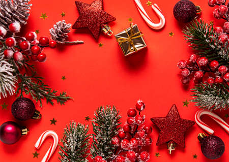 Christmas and New year background with fir branches, holly berry,  pine cones and decorations on red background. Creative flat lay, top view design with copy spaceの写真素材