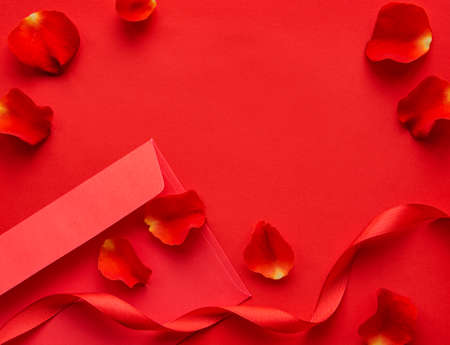 Valentines day romantic background - red rose petals, gift and envelope on a red background. Flat lay, copy space.の写真素材