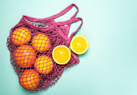 Mesh shopping bag with organic oranges on pastel green