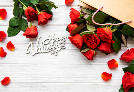 Frame made of red roses, petals   on white wooden background. Flat lay, top view, copy space.